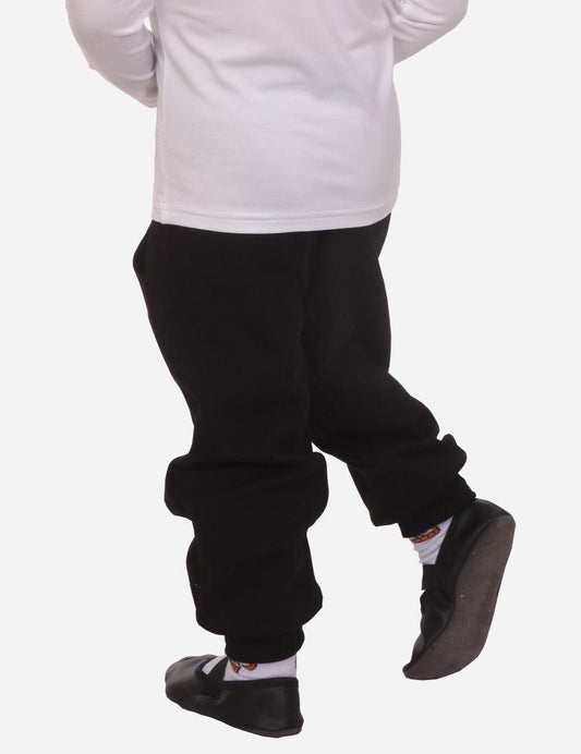Back view of a young boy in white long sleeve shirt and black cuffed pants on white background
