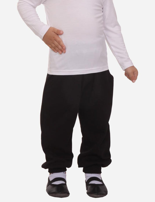 Child in white shirt and black pants with cuffs looking down and to the side, white background