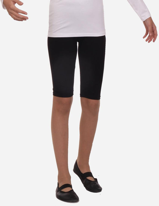 Child in white top and black capri leggings standing with side view on white background