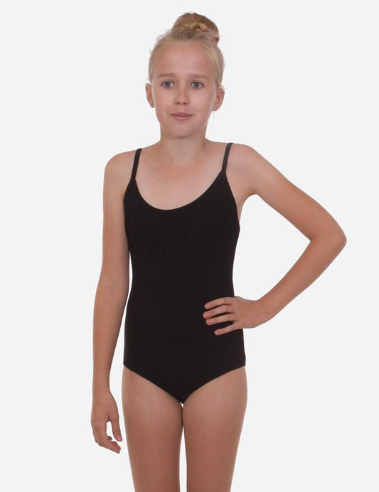 Young girl in a black leotard with straps, standing with a hand on her hip, hair styled in a bun, on a light background.