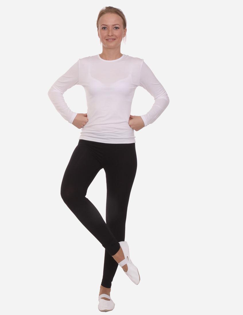 Confident woman in a long-sleeved white shirt and black leggings, hands on hips, standing on one leg, isolated on a white background