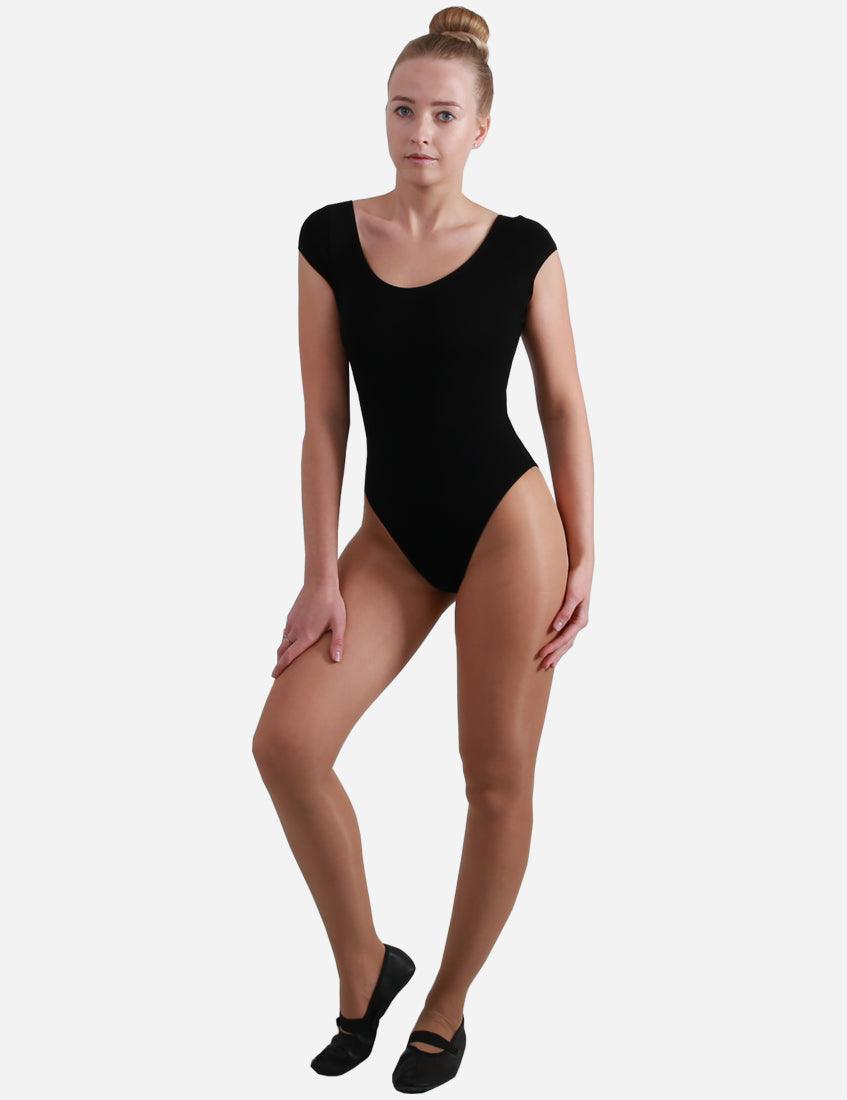 Woman in an elegant black leotard with winged sleeves, standing confidently with hands on hips and wearing ballet slippers.