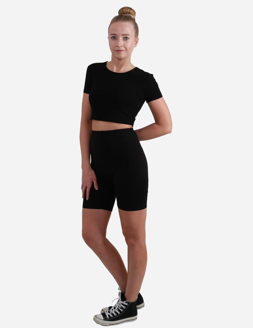Full body view of a woman in black short sleeve crop top and black leggings on white background