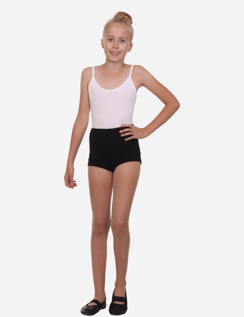 Young girl smiling in a white tank top and black shorts standing with one hand on hip against a white background