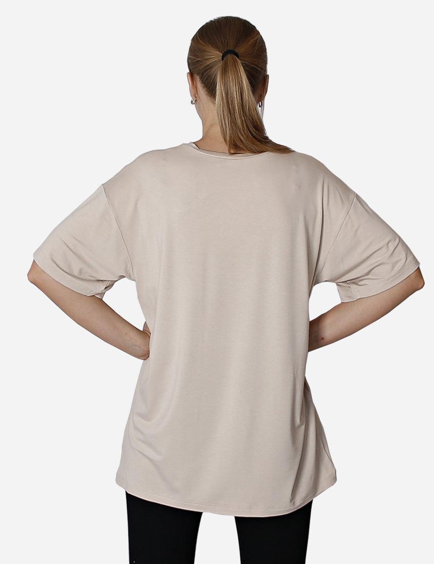 Woman from behind wearing a loose beige unisex t-shirt on a plain background.