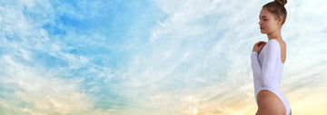 A woman is standing in a white leotard, on a beautiful, warm day, against the background of the sky.