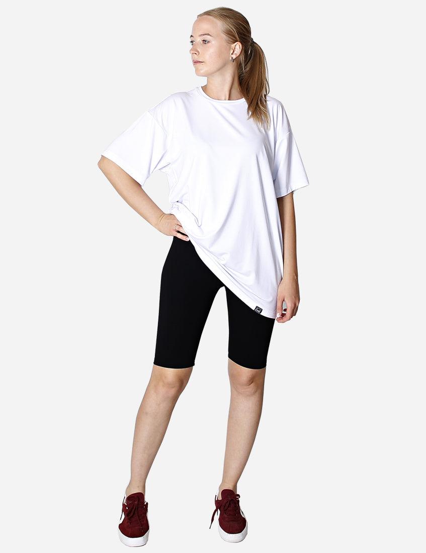 Woman posing sideways wearing white oversized t-shirt and black leggings with red sneakers