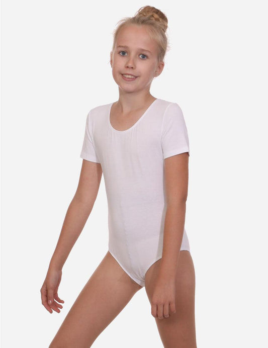 Young girl with a bun hairstyle smiling in a white short sleeve leotard, standing in a relaxed pose.