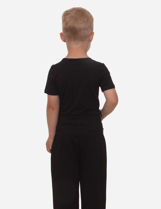 Young boy in black t-shirt and pants standing with his back turned against a white background.