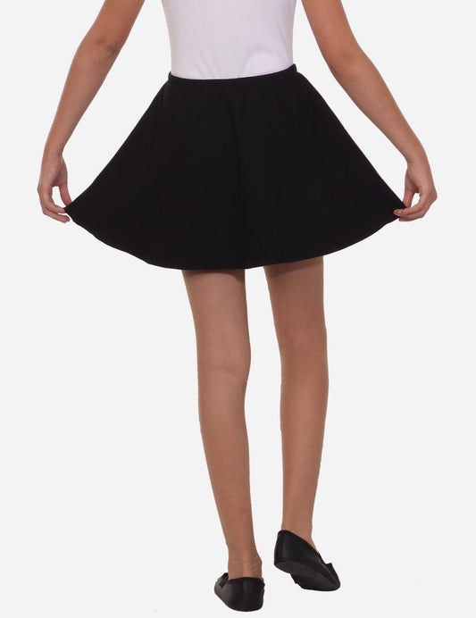 Young girl holding out a flared black skirt wearing a white tank top, black ballet flats, isolated on white background.