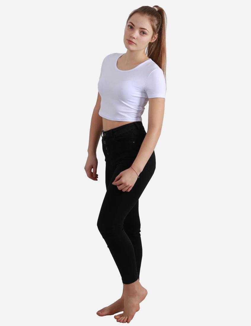 Young woman in a white short sleeve cropped top and black jeans standing with a side view on white background
