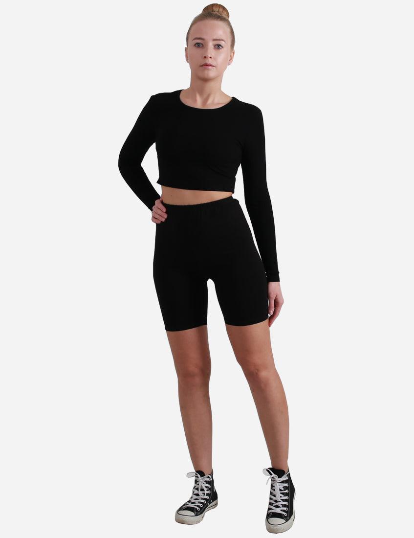 Woman in black long-sleeve crop top and cycling shorts with high-top sneakers, full body view.