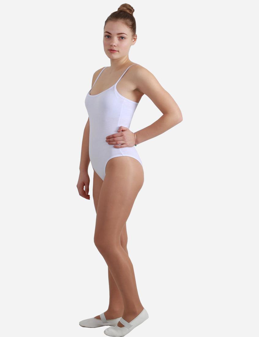 Young woman in an elegant white leotard with straps, standing in a side pose with her hair in a bun and ballet slippers.